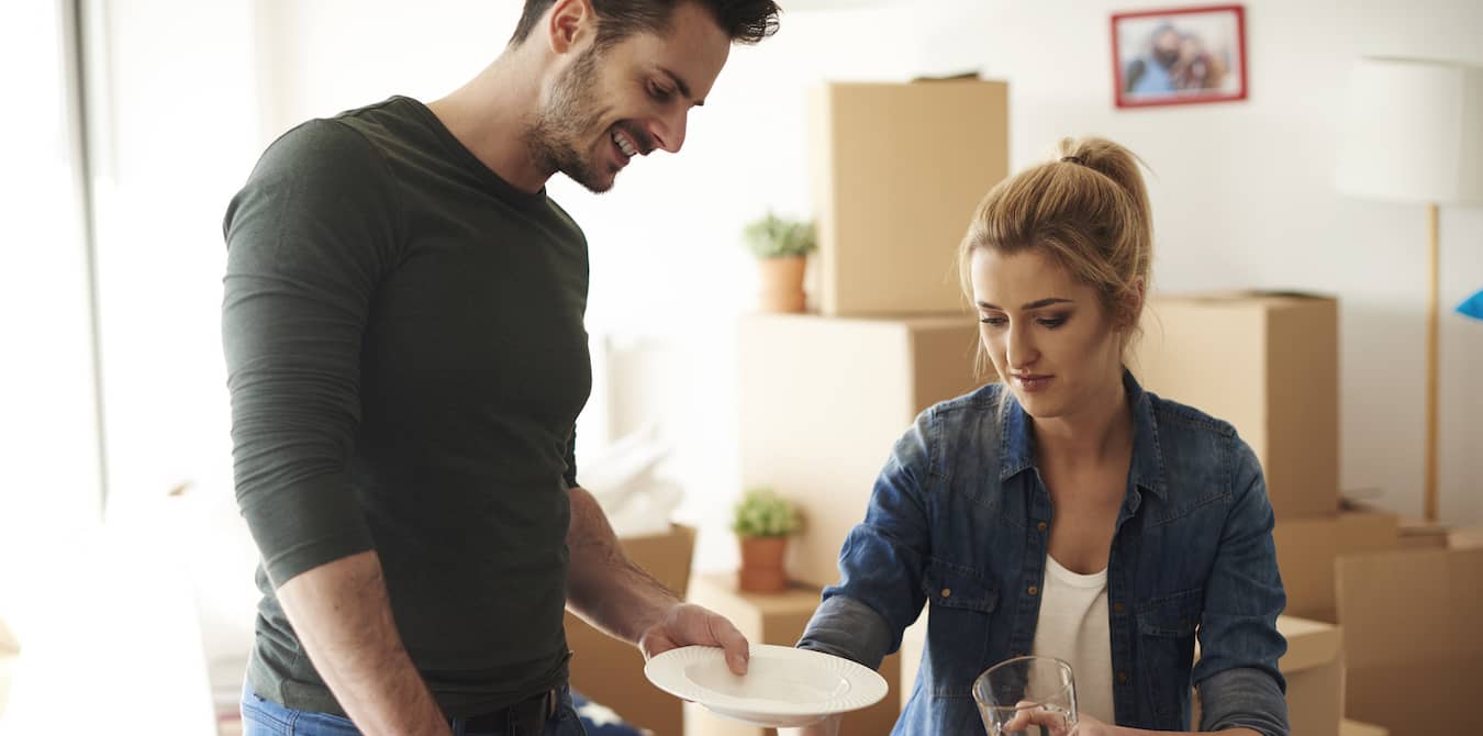 Couple packing up glasses and dishes into a cardboard box.